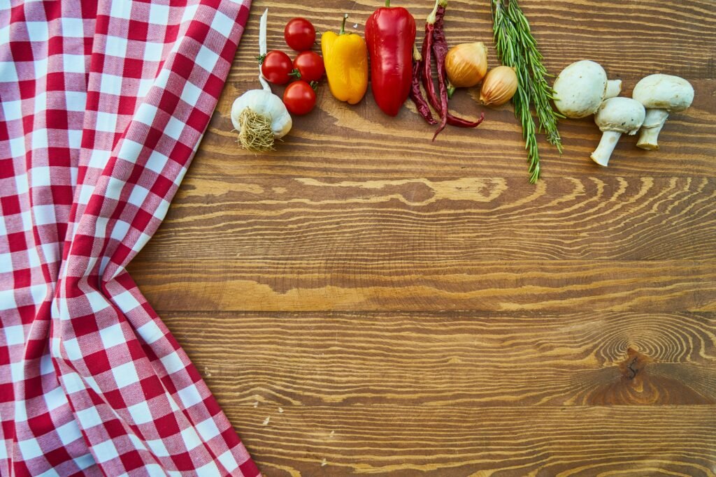 Fresh vegetables and spices on a rustic wooden table with checkered cloth.